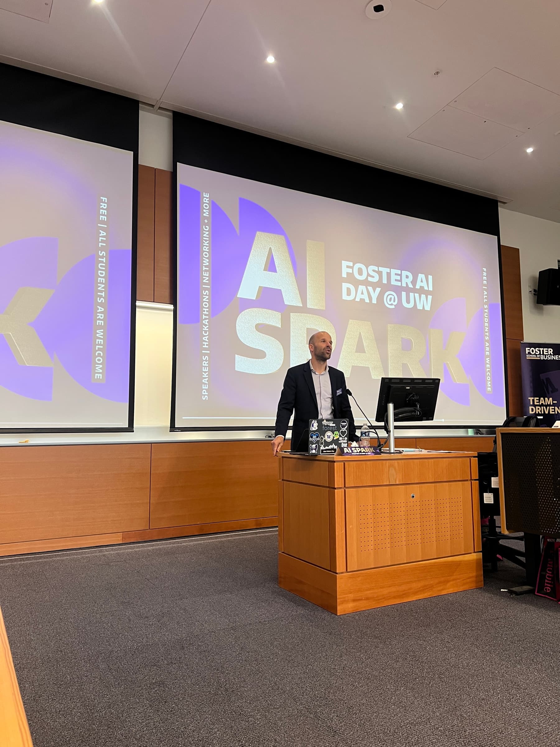 A speaker addressing the audience in front of an AI Spark presentation.