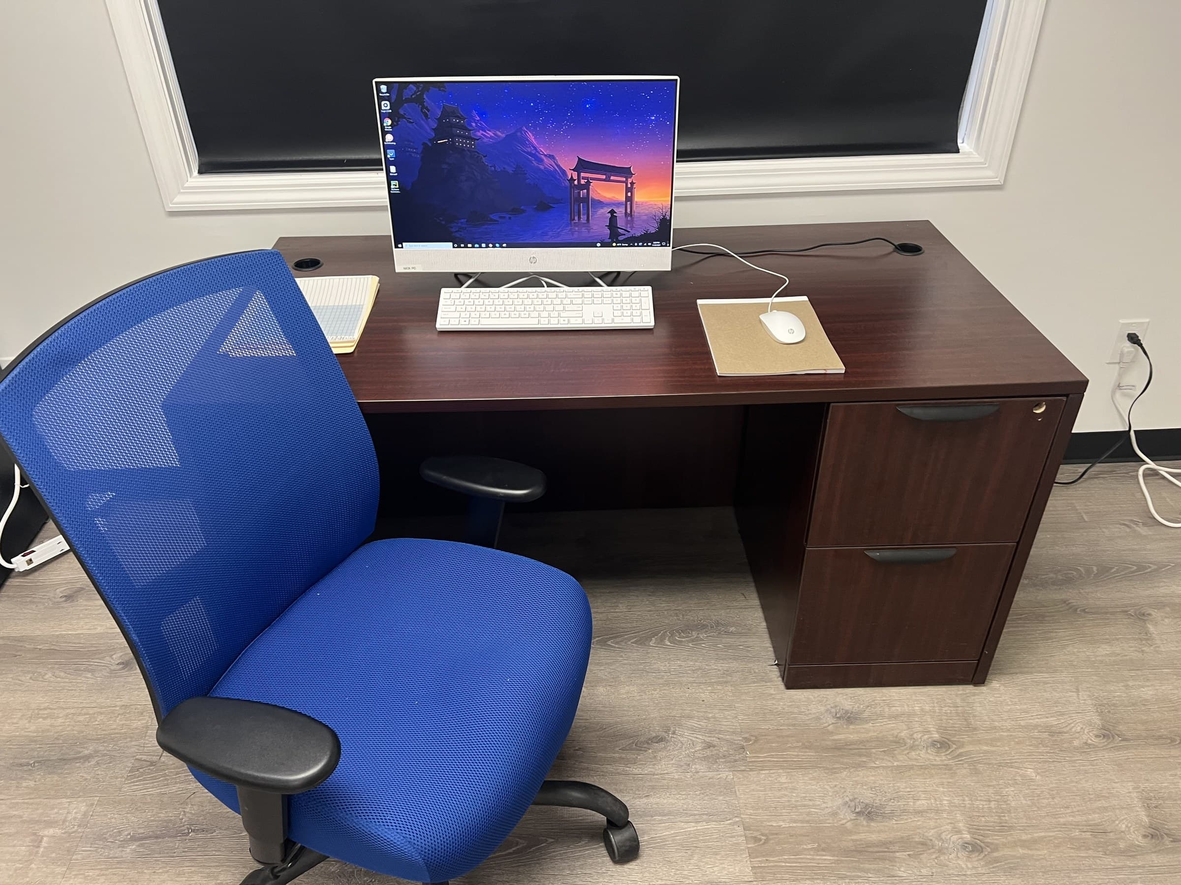 Office desk with a computer, notebook, keyboard, and blue chair.