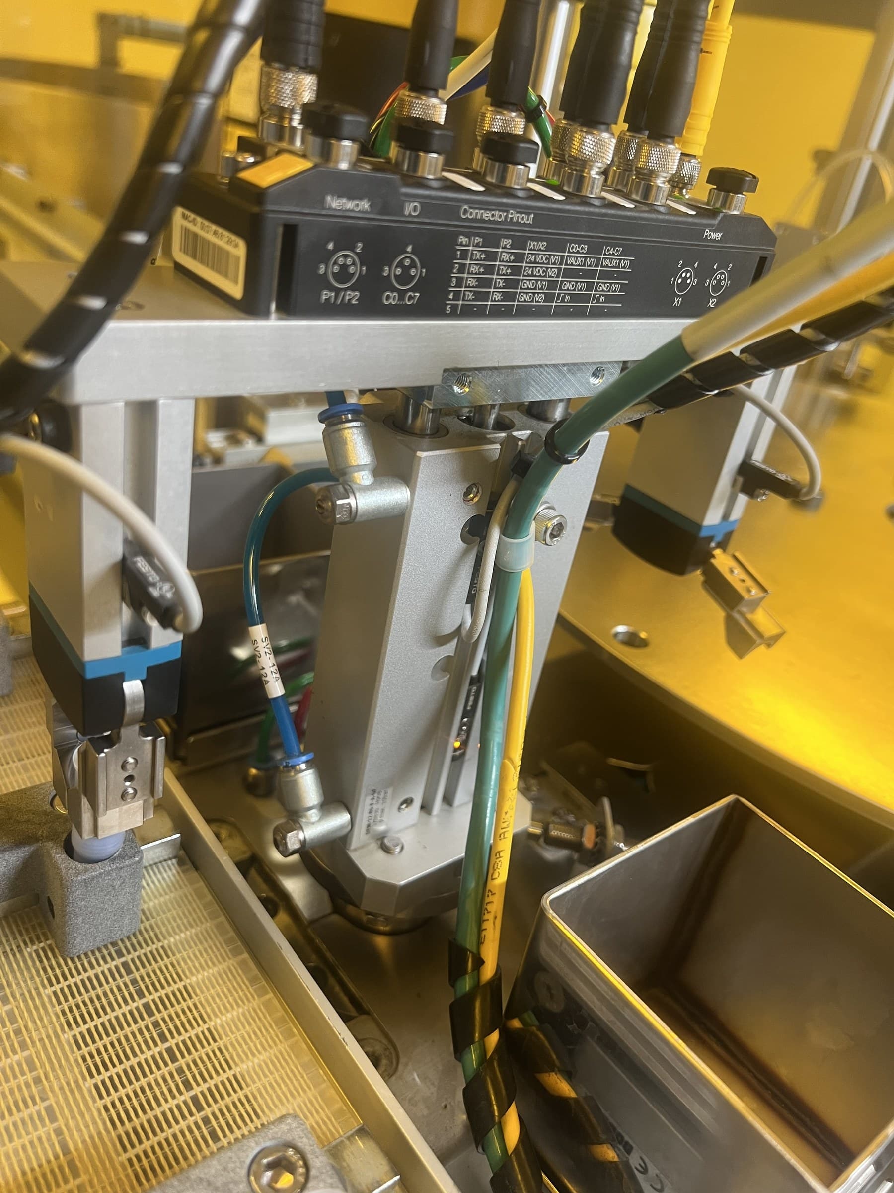 Close view of a machine assembly with pneumatic tubing, cables, and an industrial connection block.