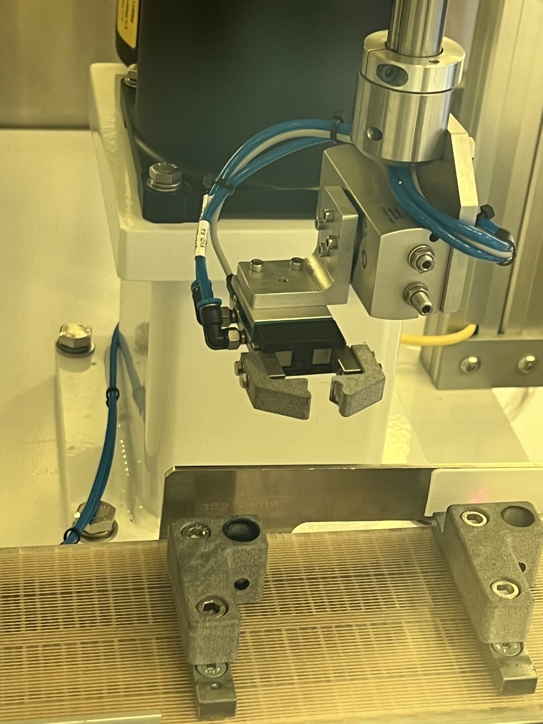 Pneumatic gripper positioned above fixtures on a conveyor.