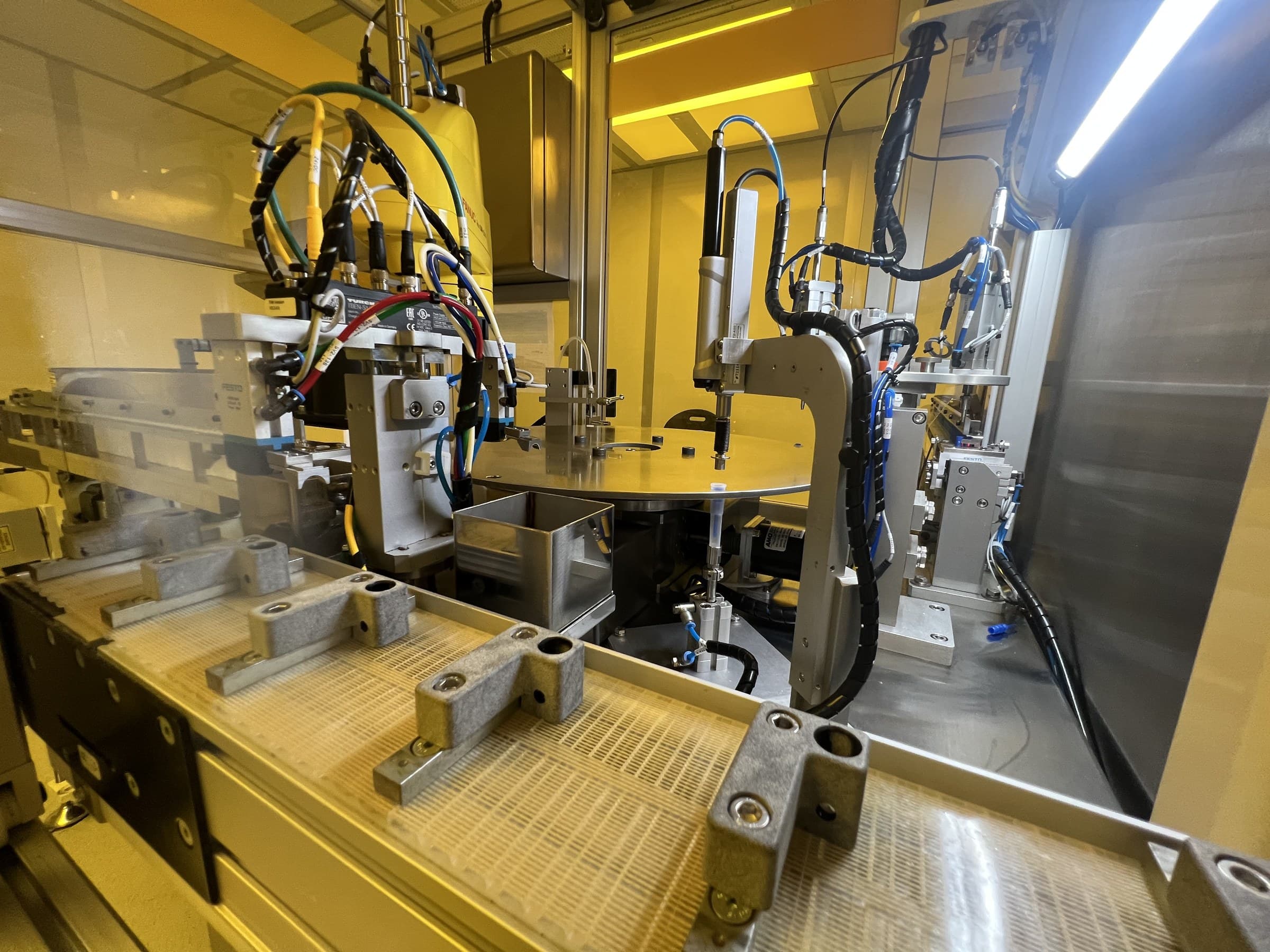 Conveyor fixtures in front of a circular machine station and pneumatic equipment.