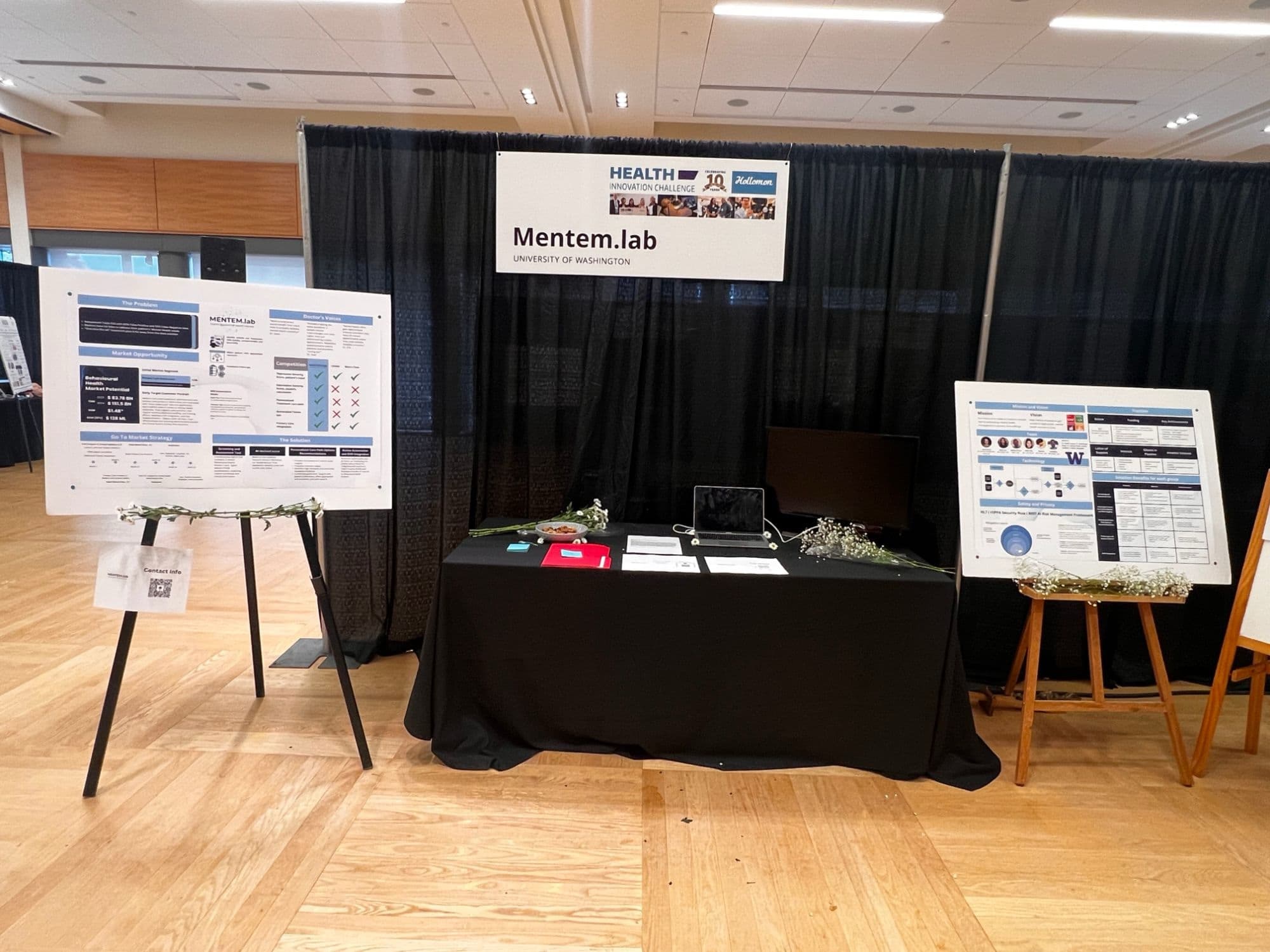 The Mentem.lab booth with two posters covering the problem, market, go-to-market strategy, solution, and traction.