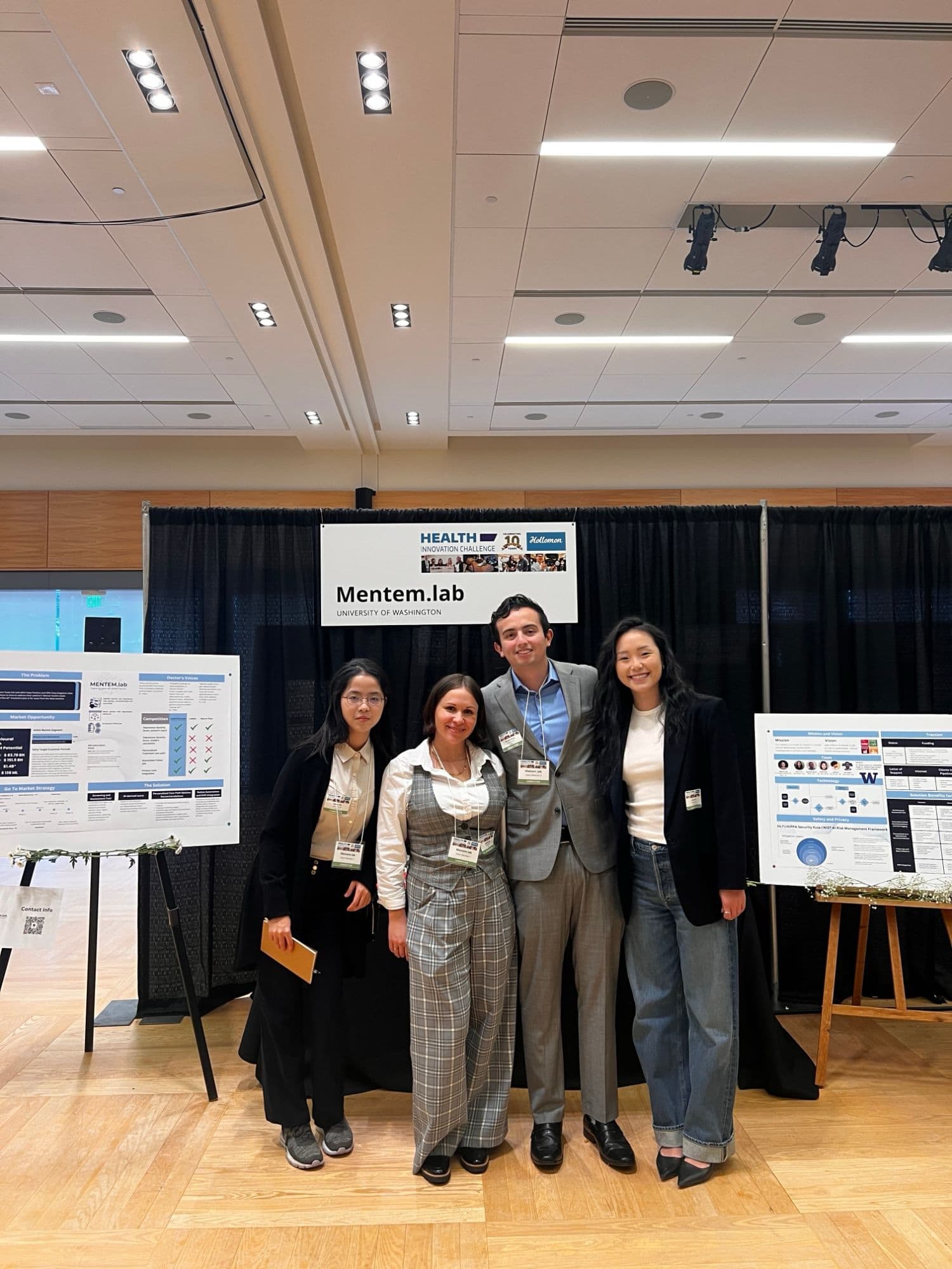 Four Mentem.lab team members at their booth under a Hollomon Health Innovation Challenge sign.