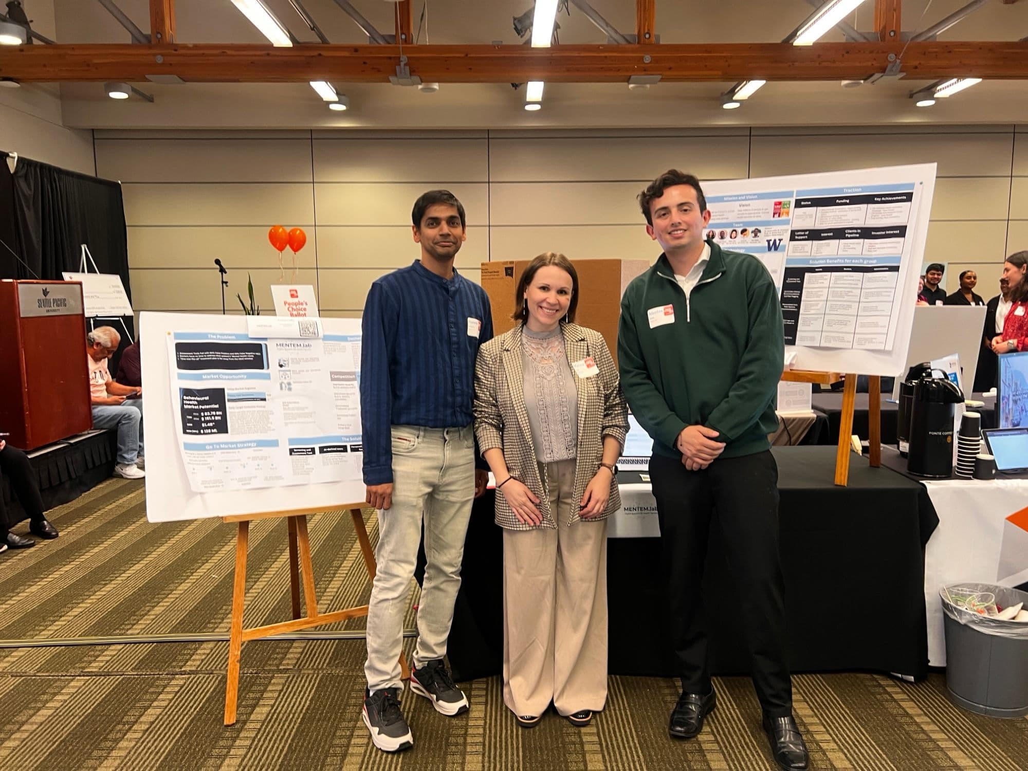 Three Mentem.lab team members standing between their posters at the Seattle Pacific University social venture competition.