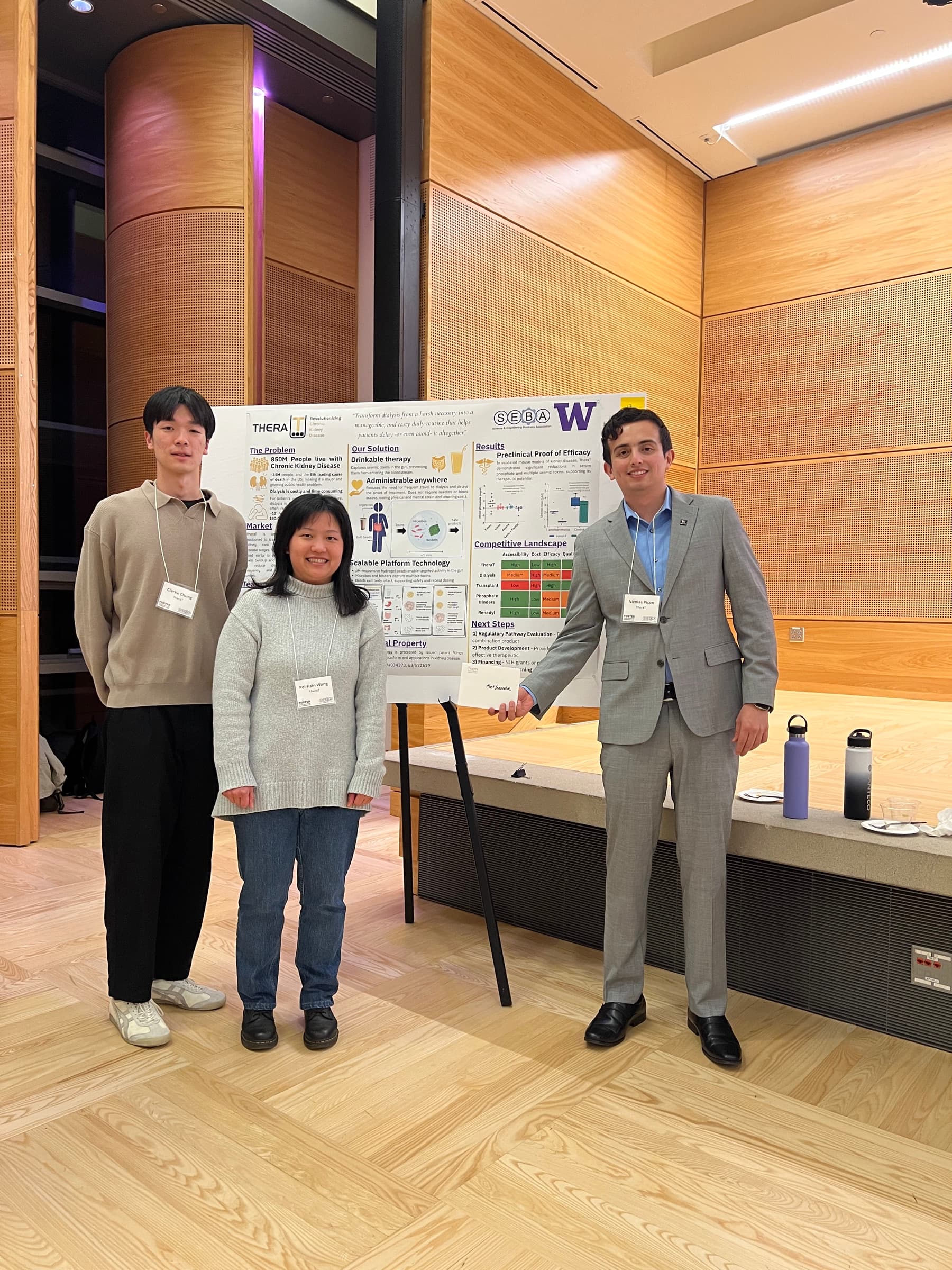 Three TheraT team members standing beside their poster at UW’s Science & Technology Showcase.
